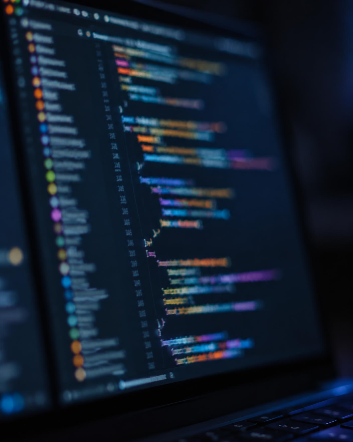 Illustrative macro photograph of program code displayed on a laptop screen with colour syntax highlighting